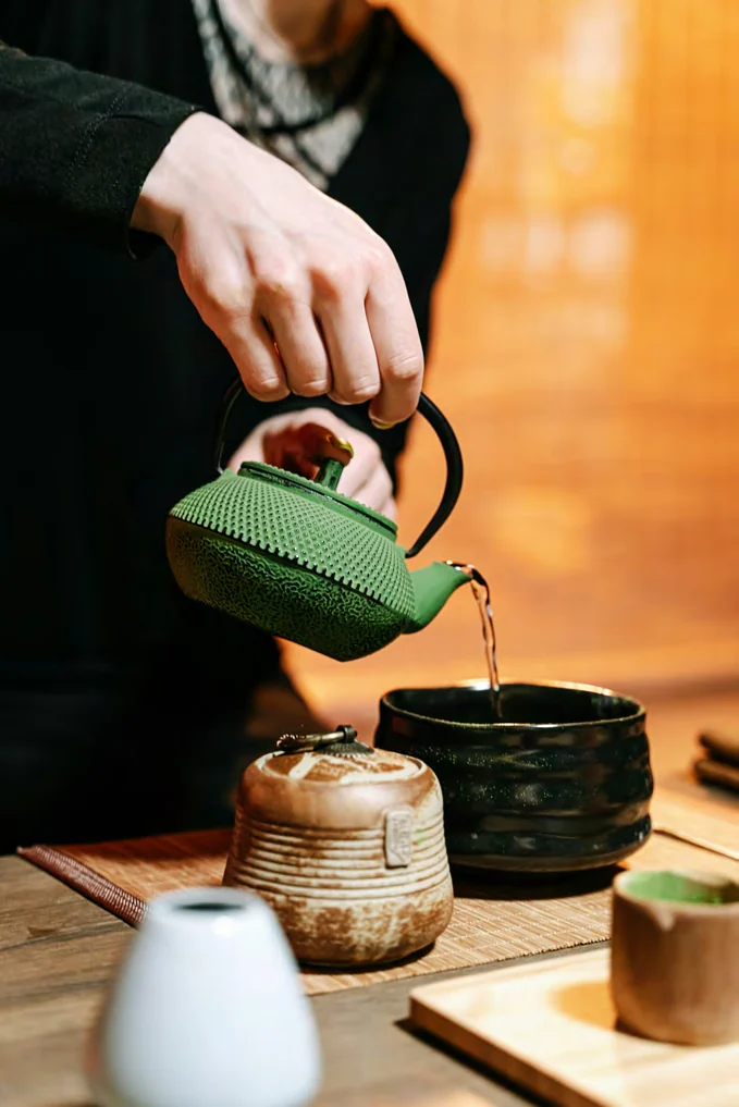 Pouring tea from a green cast-iron kyusu into a matcha bowl